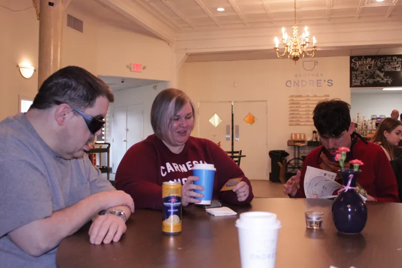 Three people sitting at a wooden table enjoying beverages.